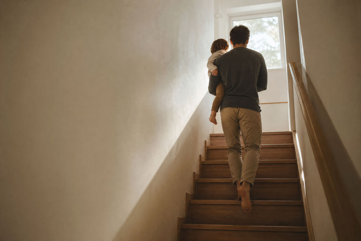 A man carrying a small child up a staircase at home